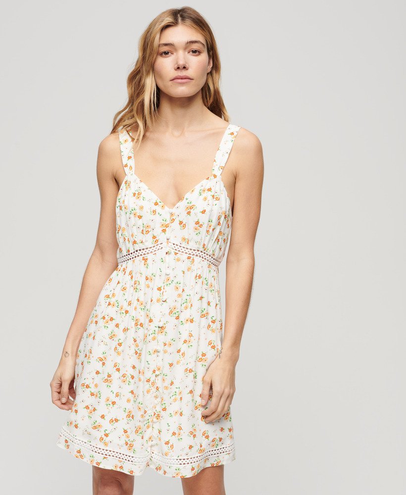 cami-jurk met v-hals en kanten afwerking in wit met een speels bloemenpatroon.