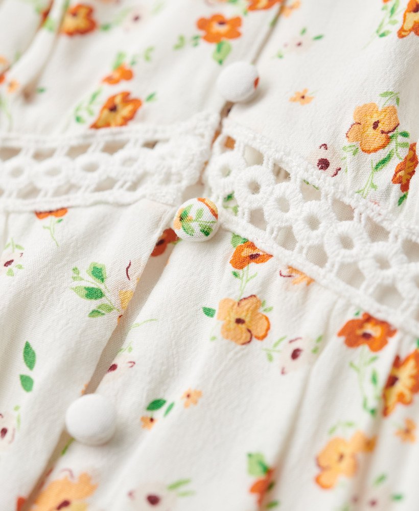 cami-jurk met v-hals en kanten afwerking in wit met een speels bloemenpatroon.