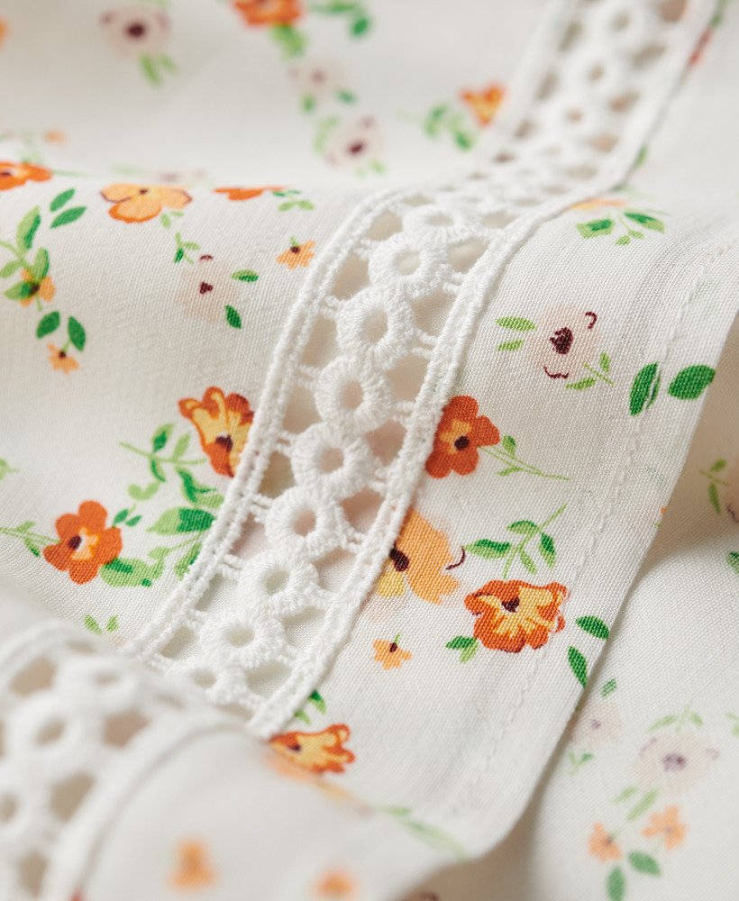 cami-jurk met v-hals en kanten afwerking in wit met een speels bloemenpatroon.